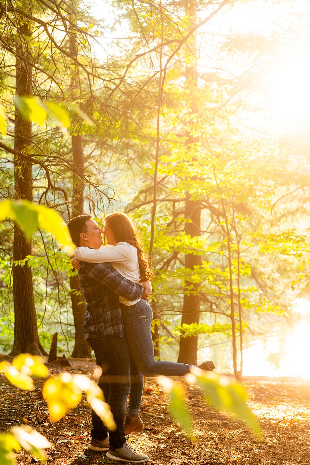 A romantic couple embraces in a sunlit forest with golden sunbeams filtering through autumn leaves at sunset.