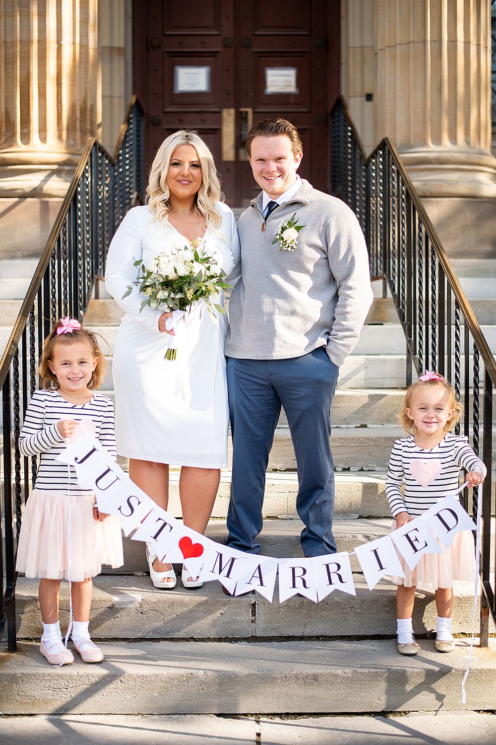 A wedding photo on church steps with two children in matching striped outfits holding a 'Just Married' banner.