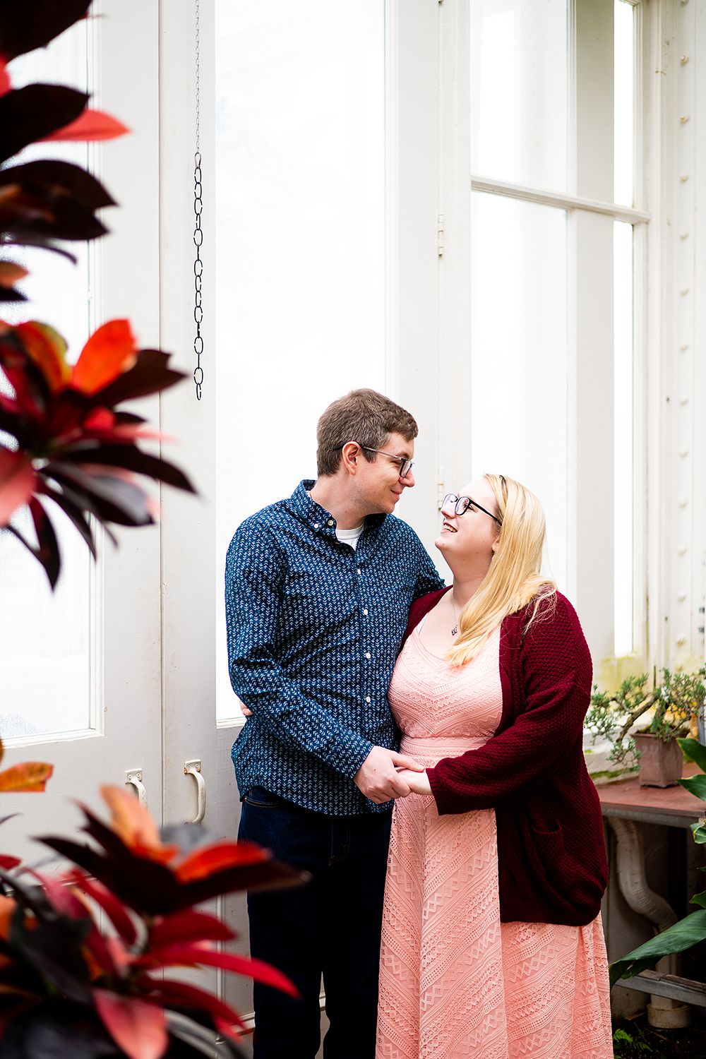 A couple shares an intimate moment in front of a window while red foliage creates a romantic frame.