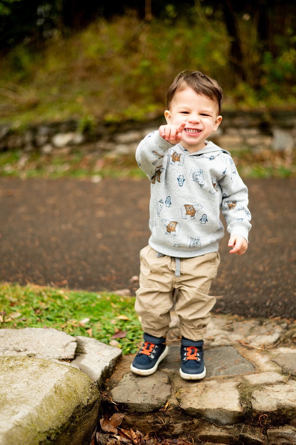 Small child in patterned sweater and navy shoes stands on stone path with excited expression.