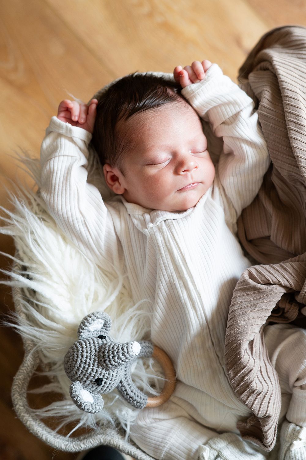 Peaceful sleeping baby in white knit sweater lying on soft furry blanket with gray knit booties nearby.