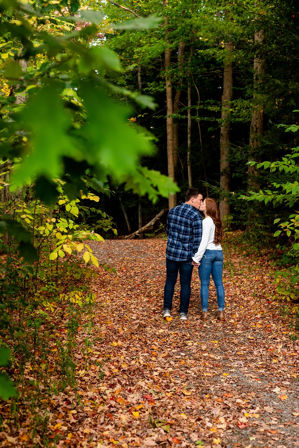 Four scenic fall photos show a couple walking together on a leaf-covered forest path surrounded by autumn foliage.