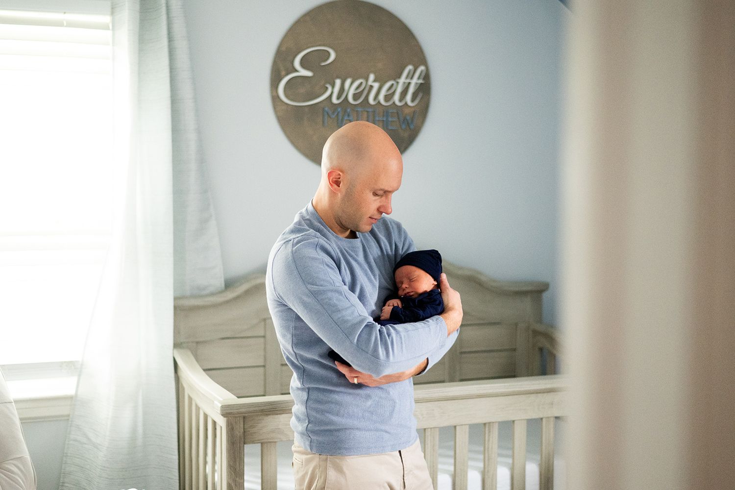 A nurturing moment with a swaddled newborn in a peaceful nursery with 'Everett' text displayed on the wall.