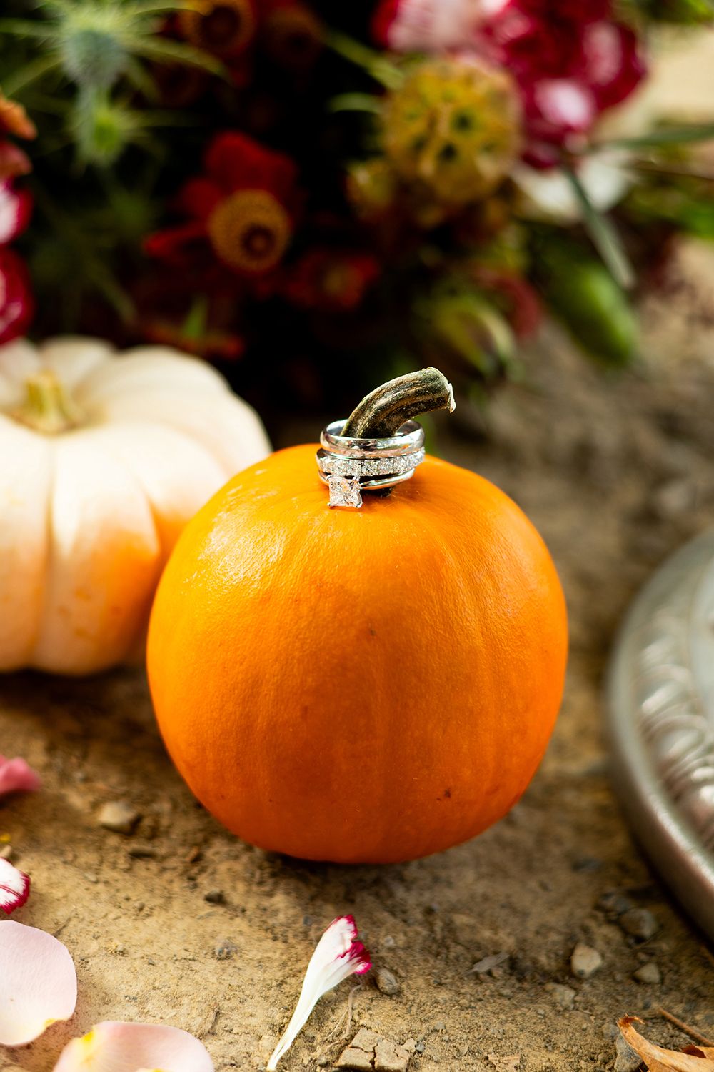 Diamond engagement ring delicately placed on top of a bright orange pumpkin with floral decor in the background.
