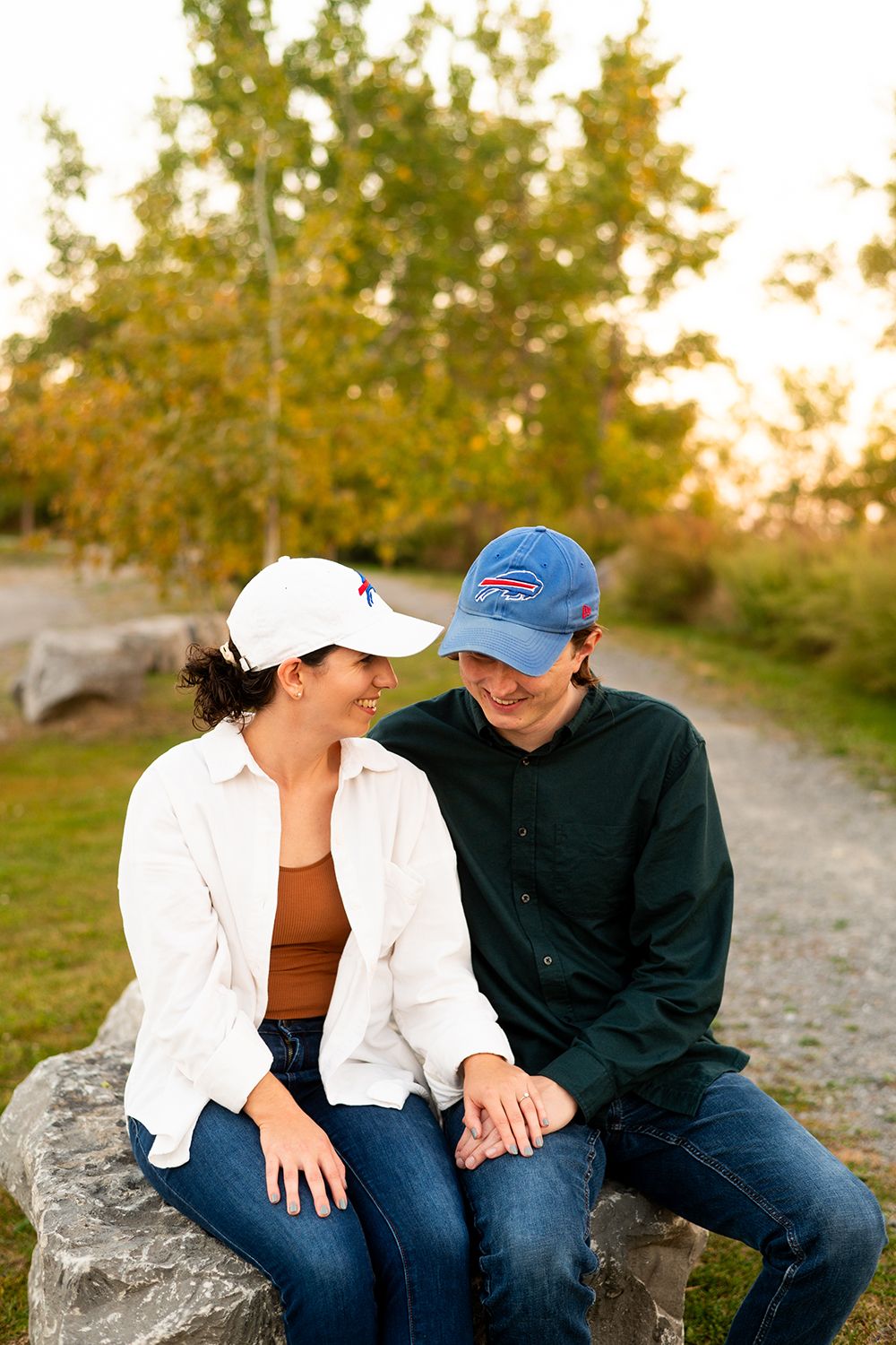 A couple sits together on rocks during golden hour autumn photoshoot in casual attire.
