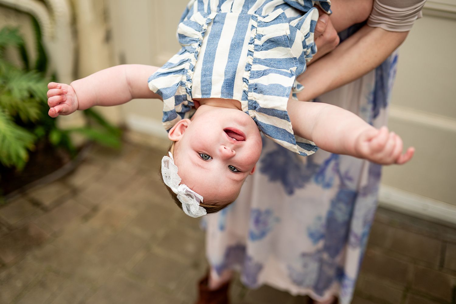 A baby wearing a striped romper plays with their bare feet while sitting on outdoor steps.