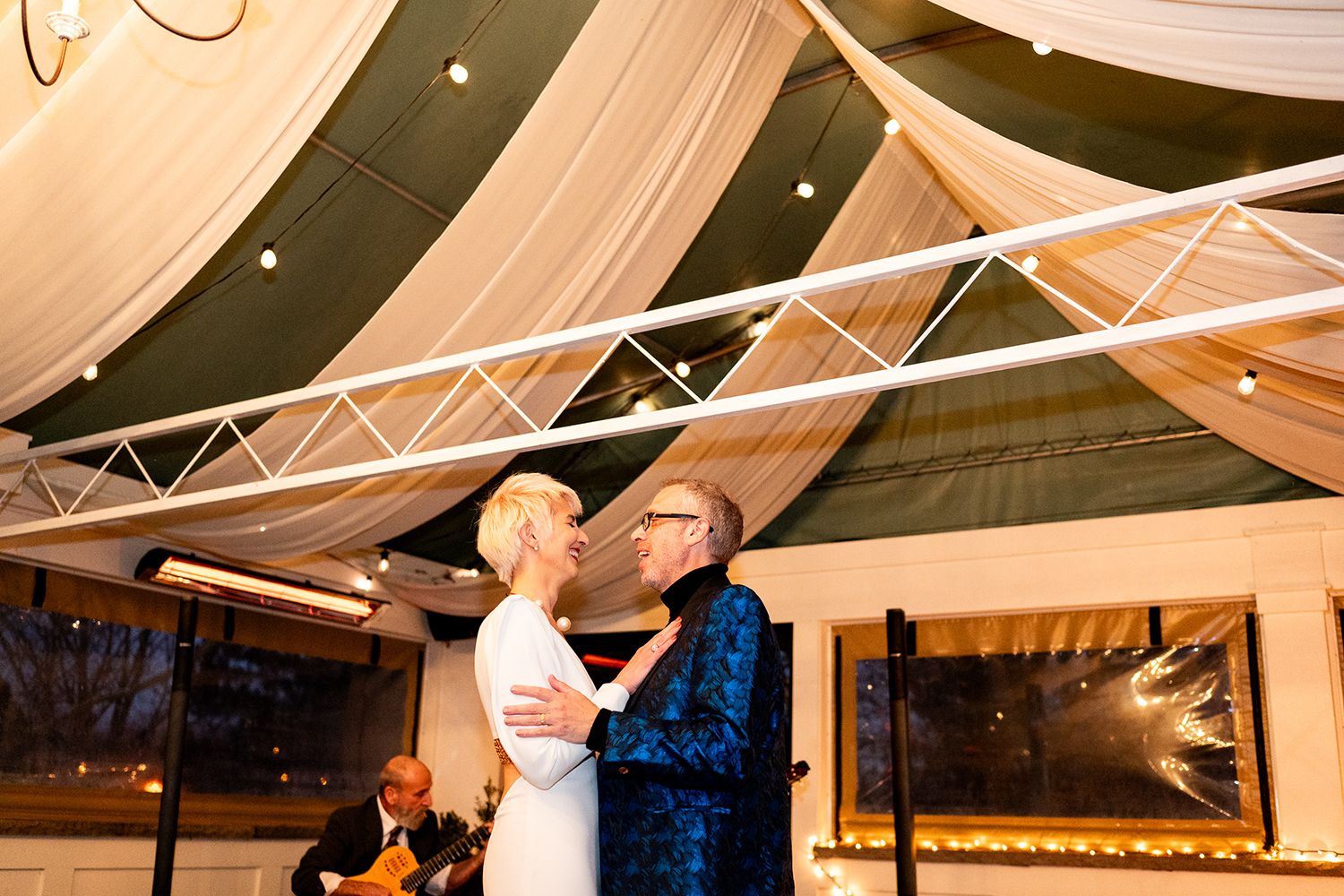 A couple shares a romantic moment during their first dance under draped fabric and trusses at an indoor reception venue.