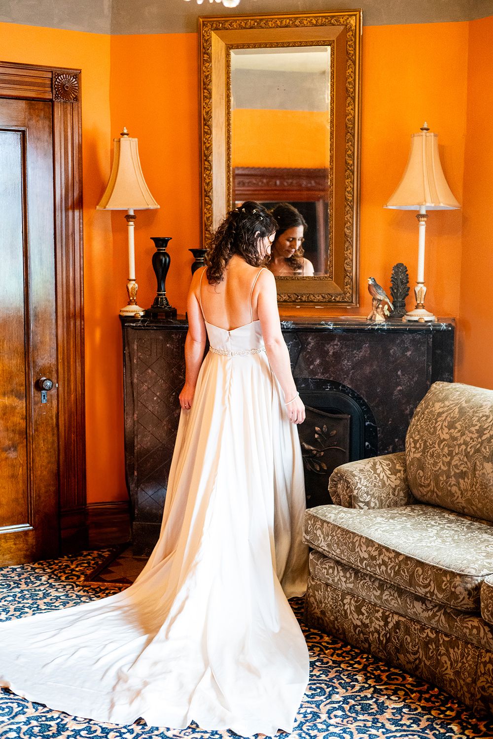 A white wedding dress with long cathedral train displayed against vibrant orange walls in a bridal suite.