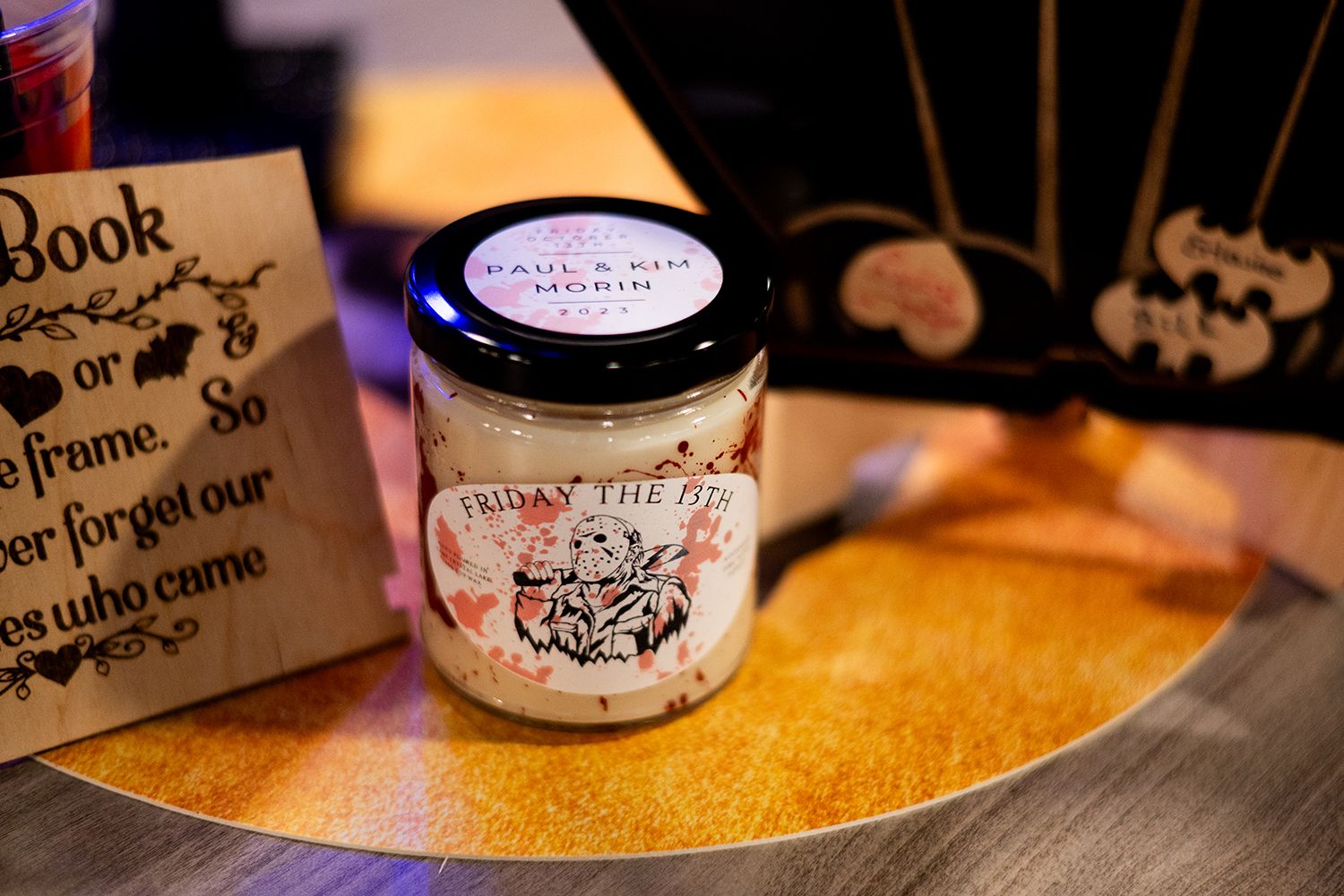 A vintage-style candle jar with an ornate label sits on a golden surface next to a decorative sign.