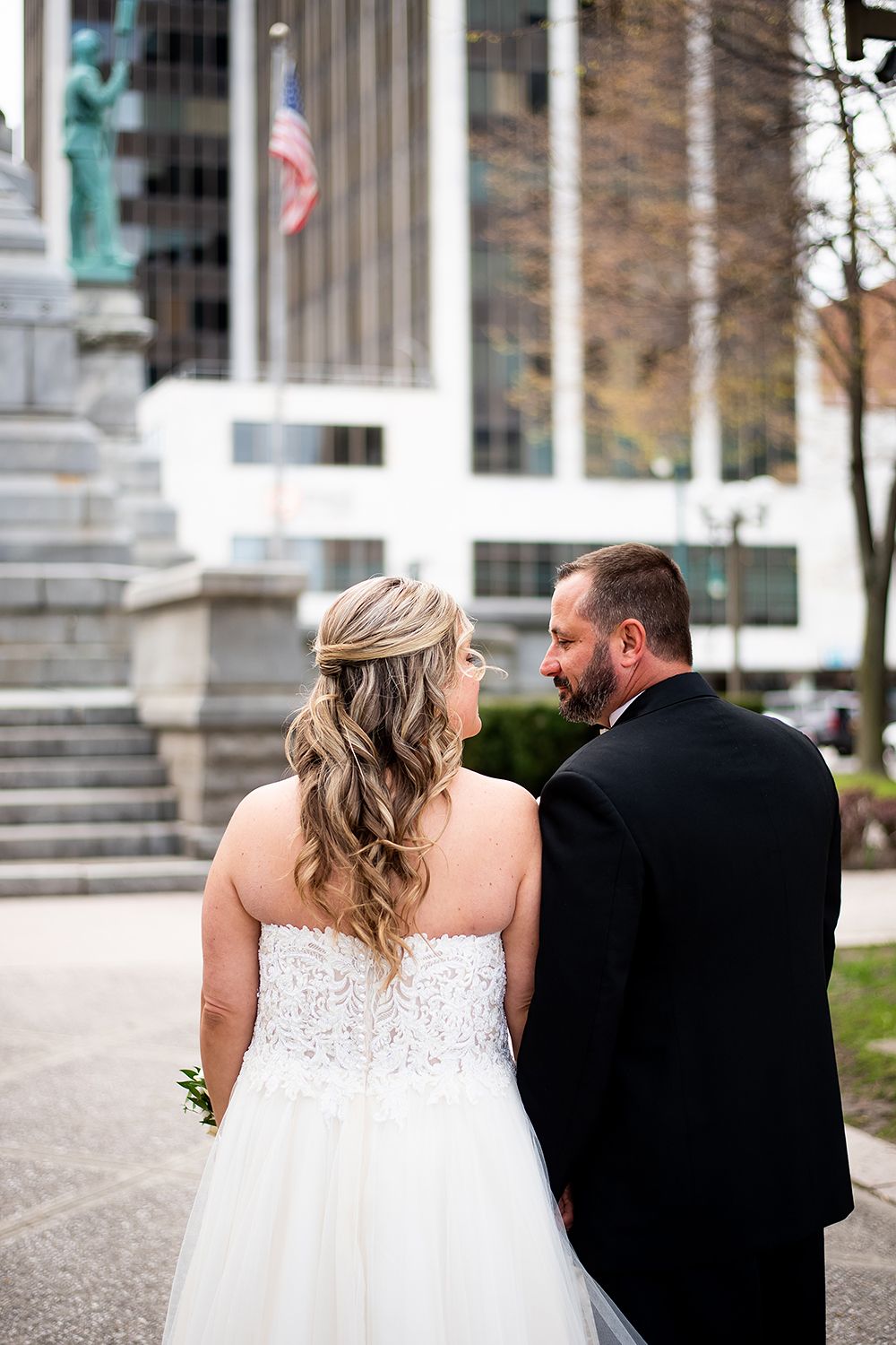 Wedding couple walking together past decorative stone columns with patina-colored statues at their tops.