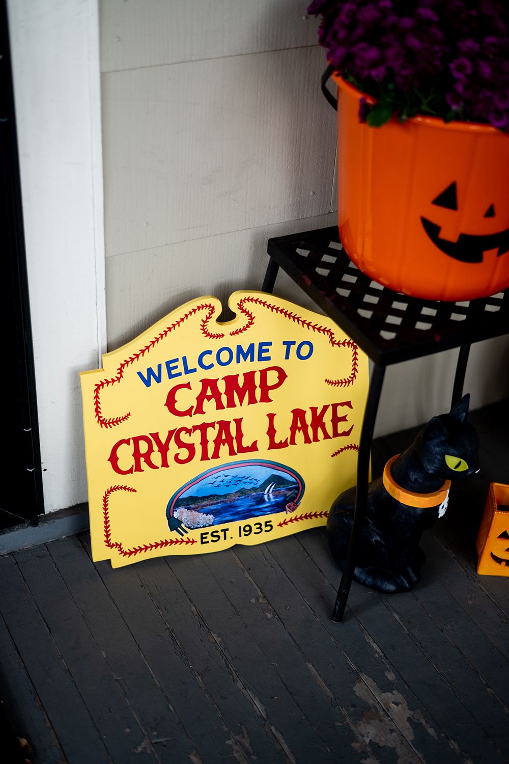 A Halloween-themed display with a Camp Crystal Lake sign, orange jack-o-lantern planter, and spooky decorations on dark flooring.