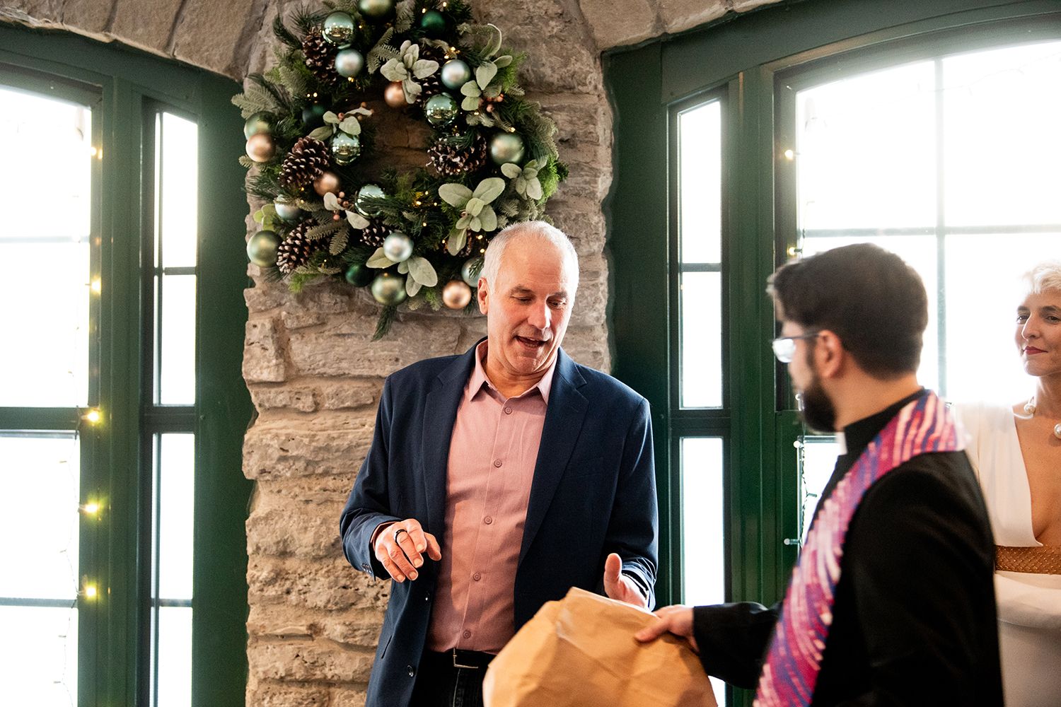 Guests interact during a social gathering beneath an elegant floral wreath and stone archway.