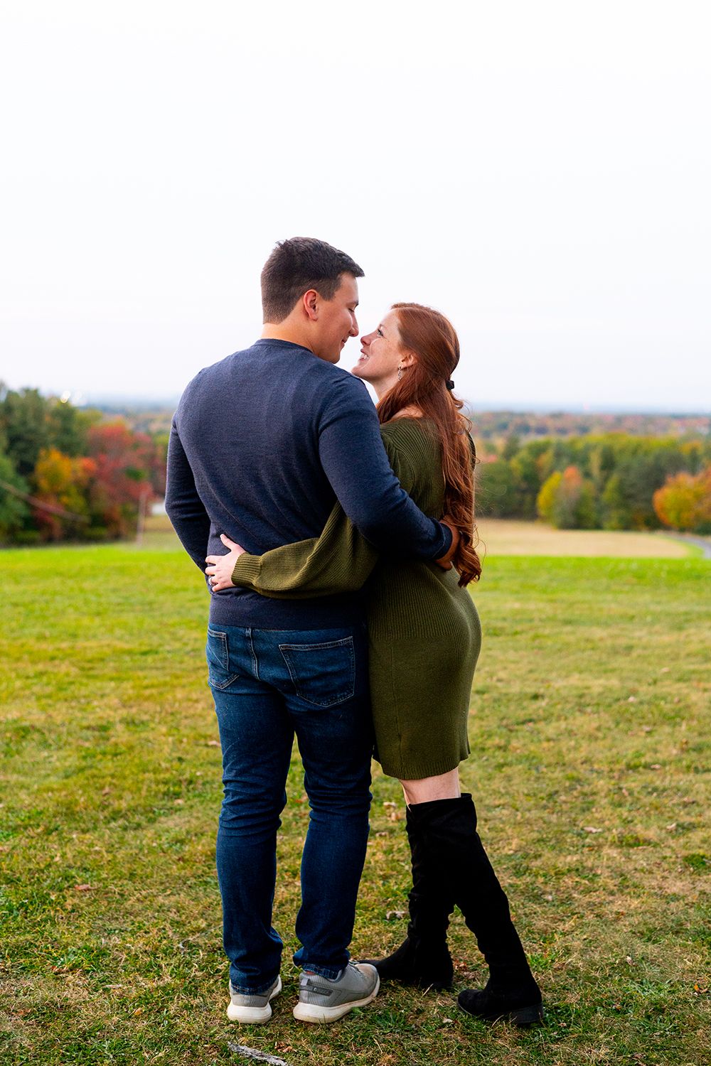 A couple enjoys a romantic moment together in a scenic autumn field with colorful fall foliage in the background.
