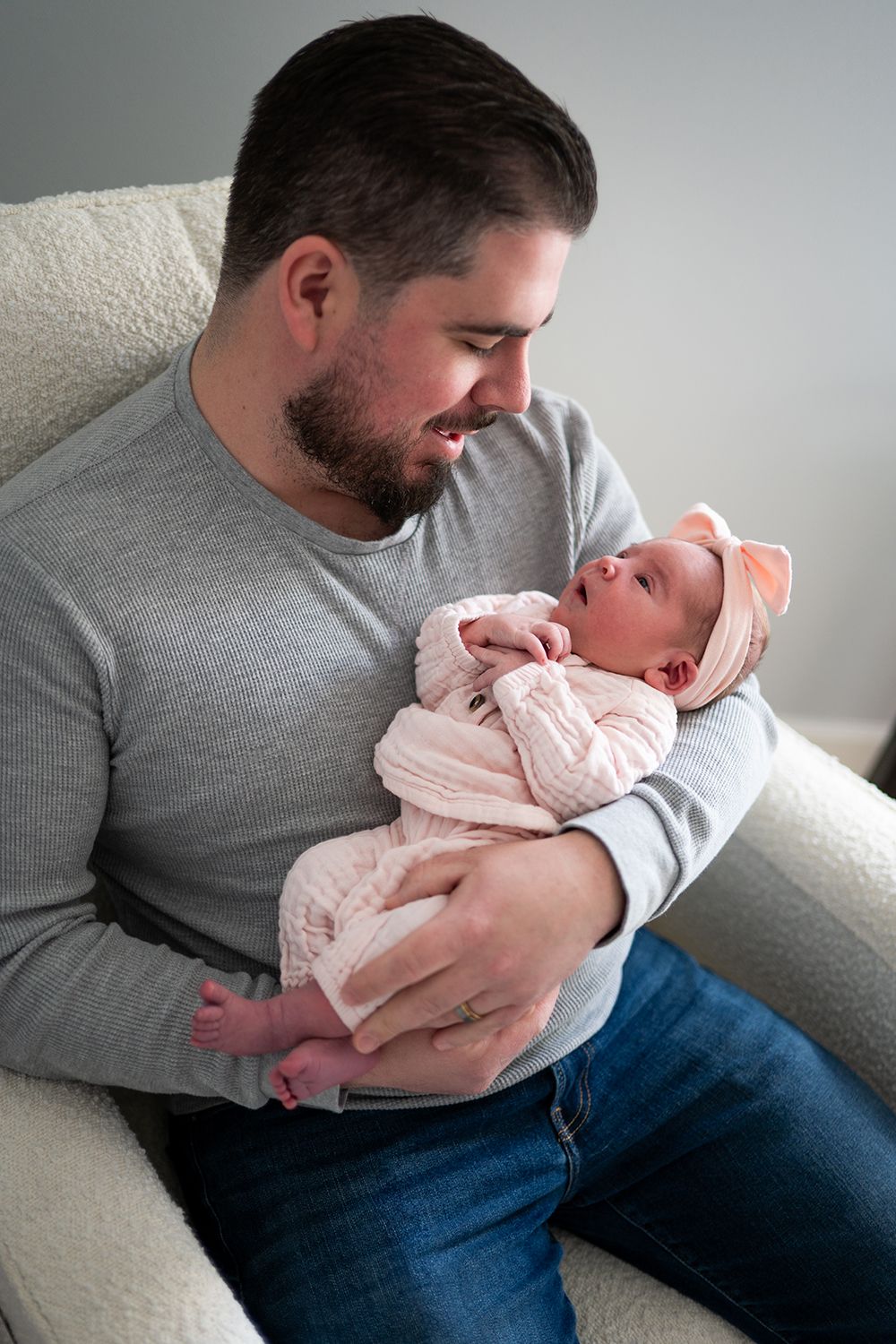 Parent tenderly holding and gazing at newborn baby while sitting on couch in gray sweater and jeans.