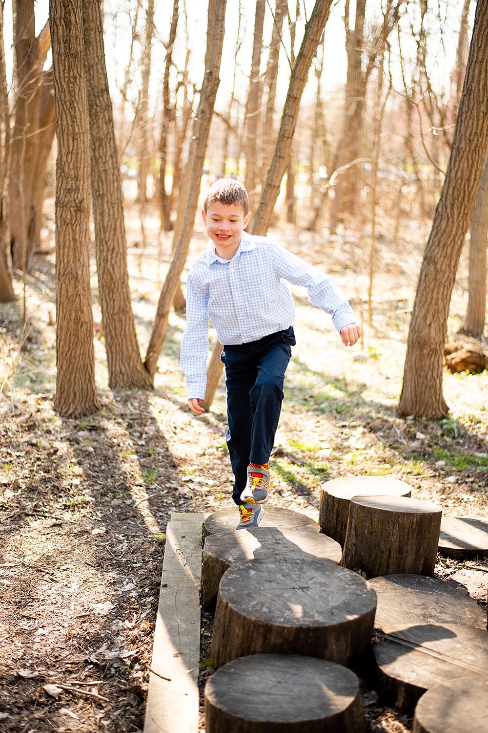Active pose jumping between wooden stumps in wooded area wearing checkered shirt.