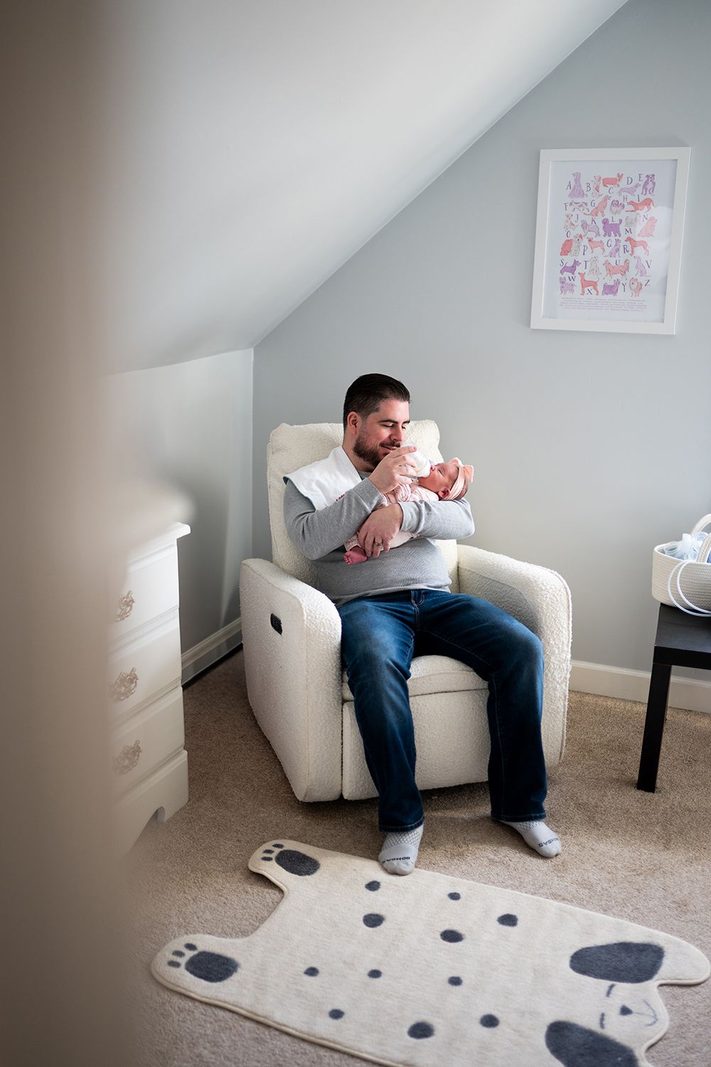Parent sits in cream recliner holding newborn while nursery decor features animal print on wall.