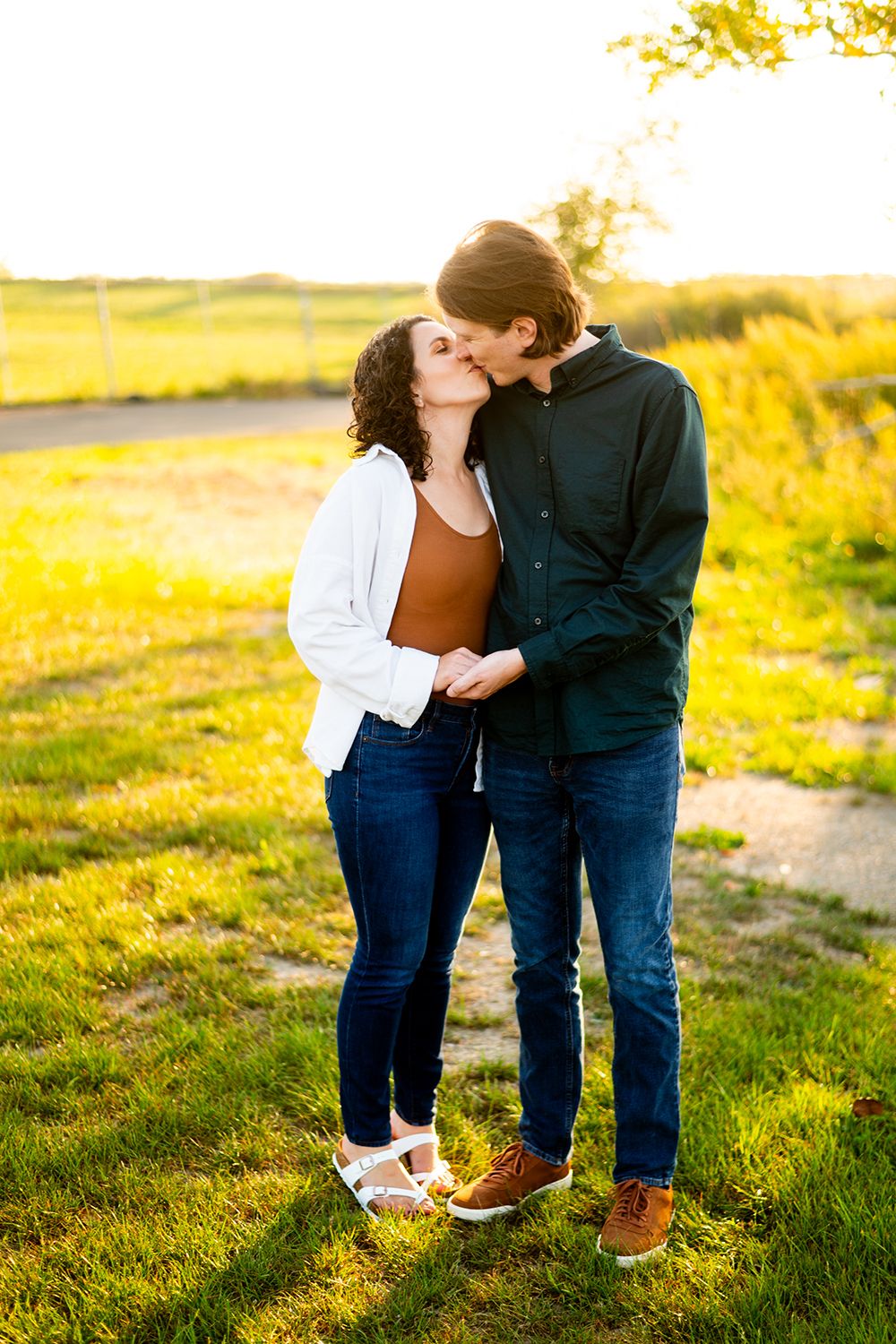 A couple shares an intimate moment in a sunlit meadow wearing jeans and casual attire at golden hour.