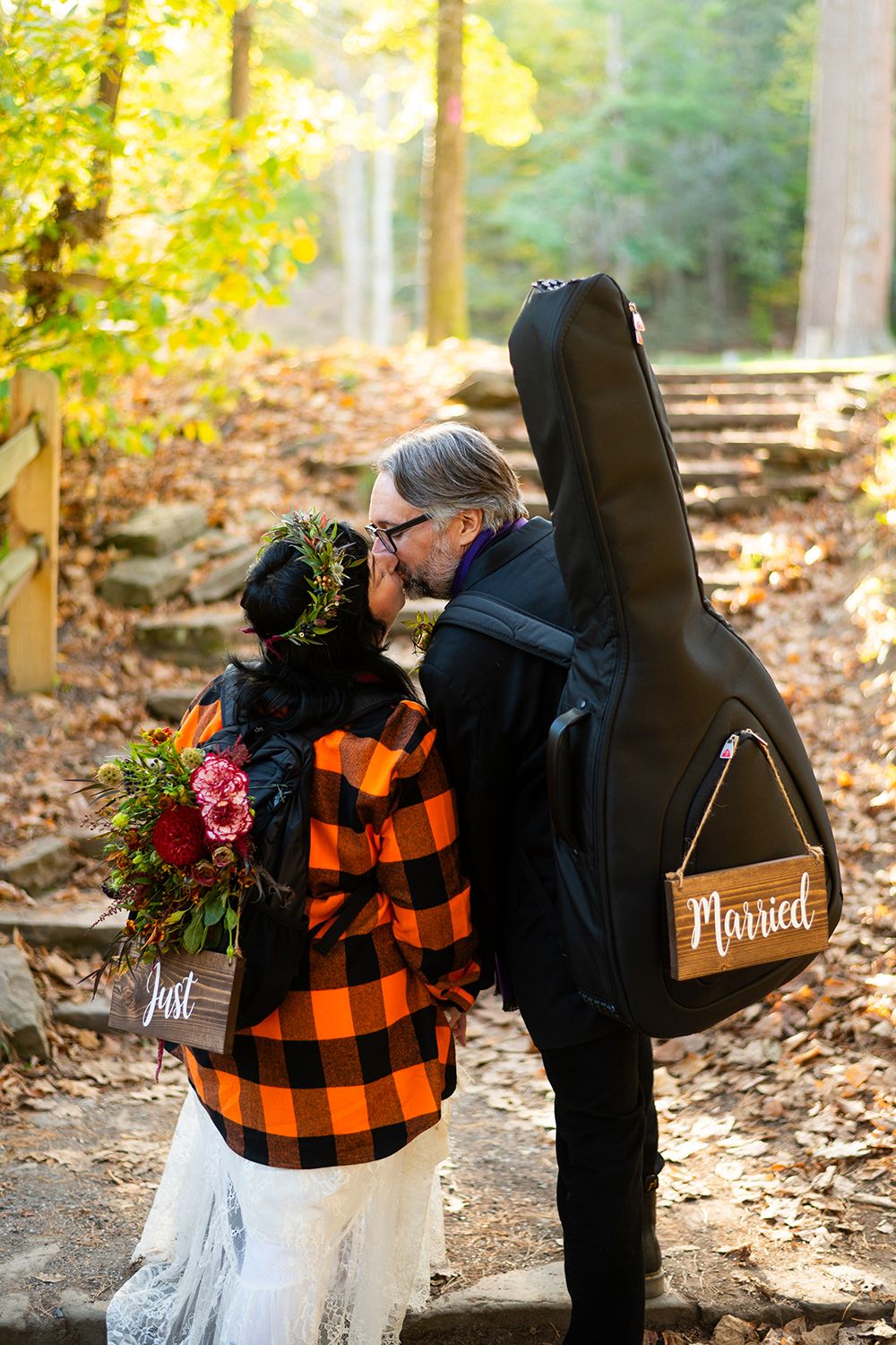 Couple in autumn attire share a romantic moment in a sunlit forest with plaid flannel and guitar case props.