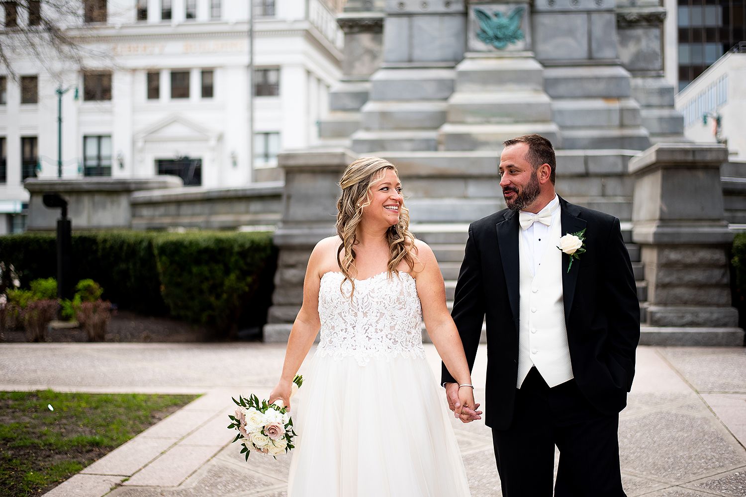 A happy couple in formal wedding attire poses together at various locations around an elegant stone building.