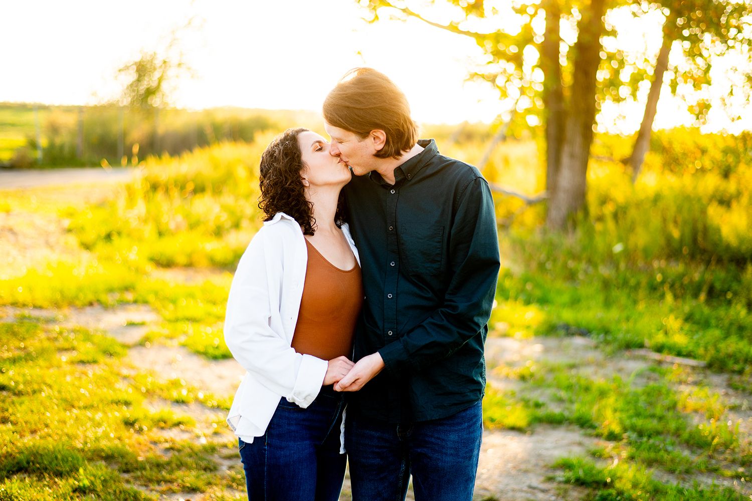 Two people share an intimate moment together in a golden sunlit field at sunset.