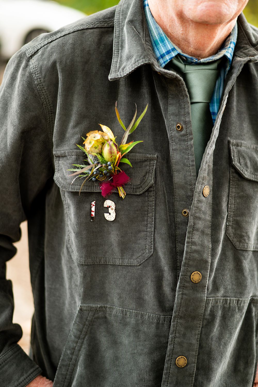 A green military-style jacket features a boutonniere with yellow roses and burgundy flowers pinned to the chest pocket.