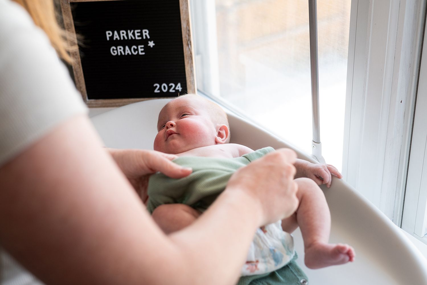 Baby on changing table with letterboard displaying Parker Grace 2024 in background.