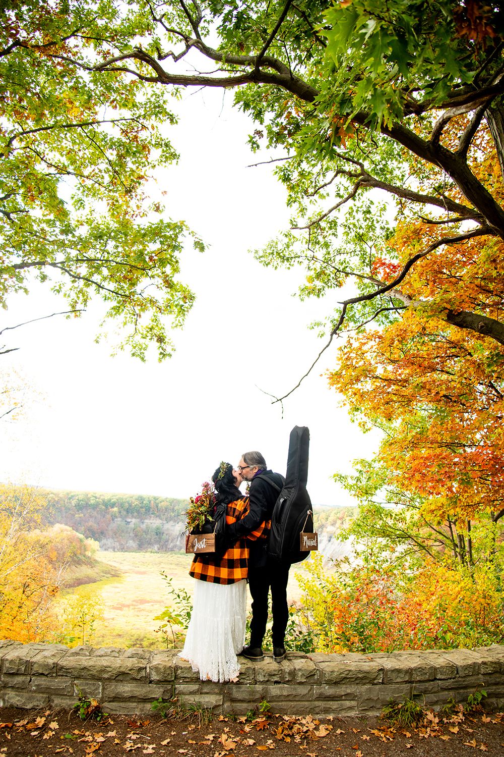Couple admiring scenic autumn landscape from stone wall overlook surrounded by colorful fall foliage.