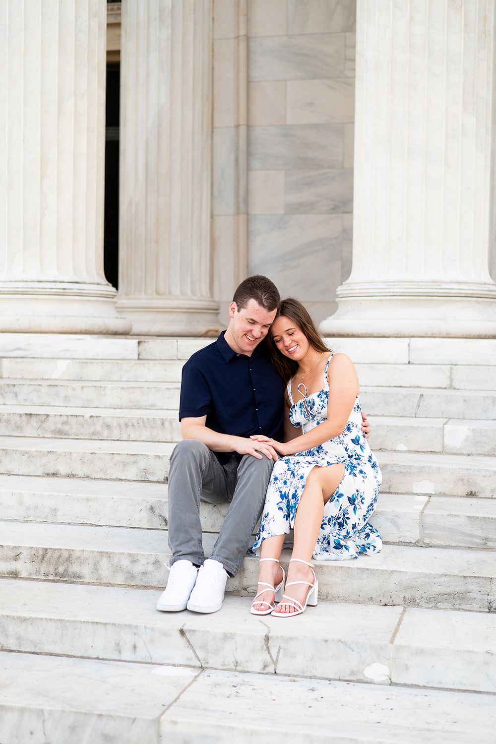 A couple sitting and talking on white marble steps shares a tender moment in a romantic engagement photo.