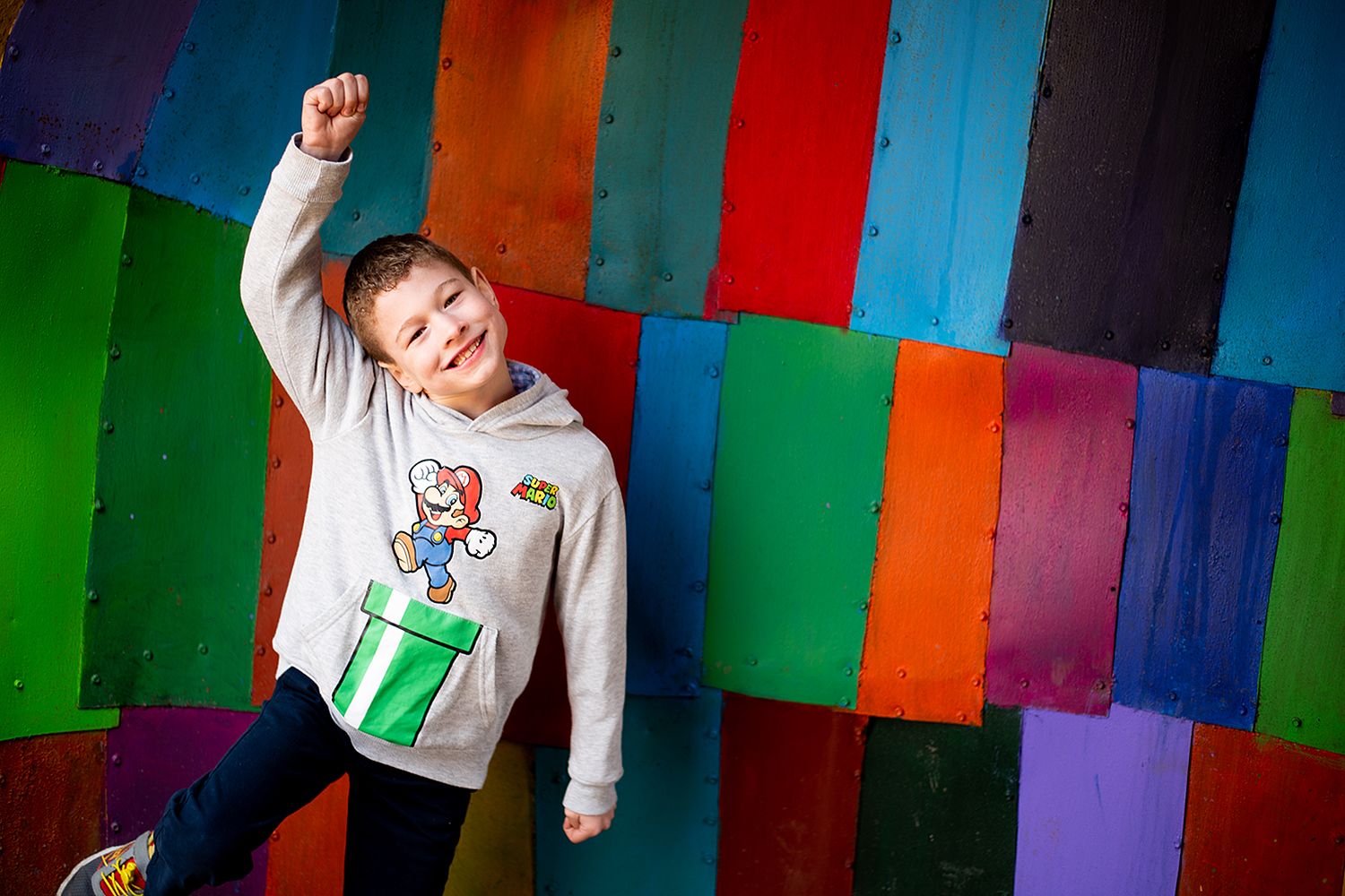 A playful photo against a vibrant rainbow-colored wall backdrop featuring a Mario-themed sweatshirt.