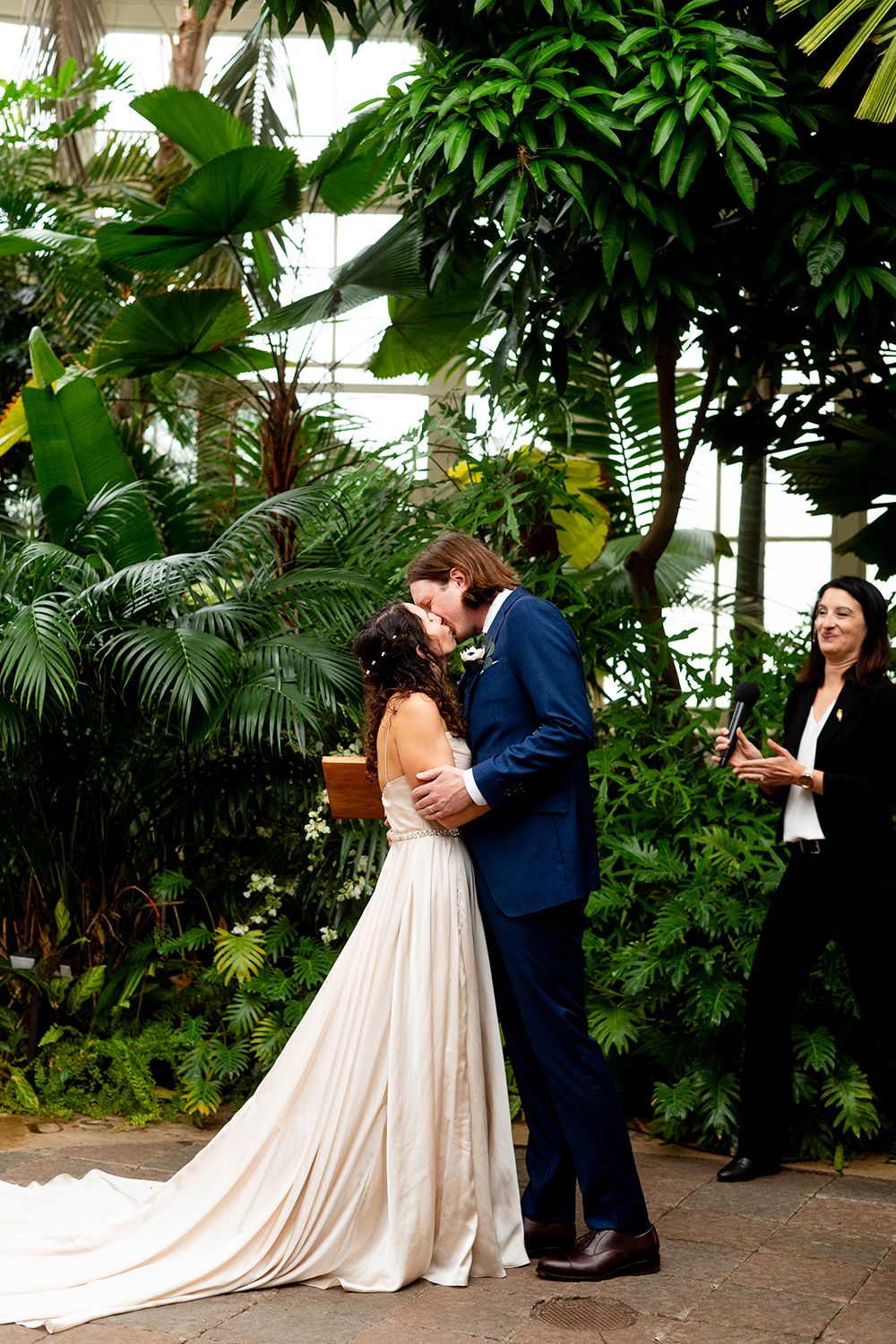 A romantic dance sequence captured inside a lush tropical greenhouse with palm fronds and exotic plants.
