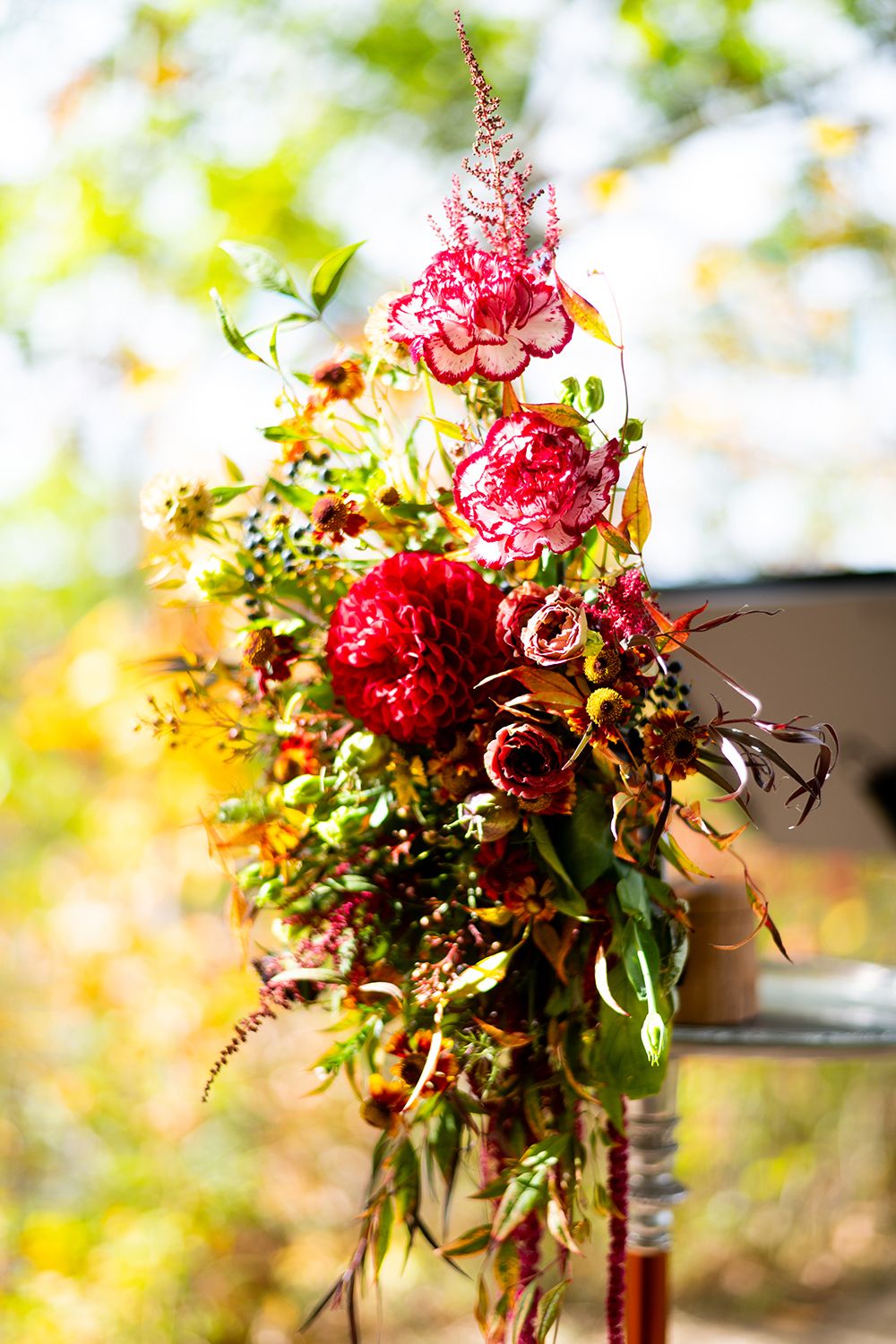A romantic bouquet of vibrant red roses and greenery arranged in a rustic style with blurred golden bokeh background.