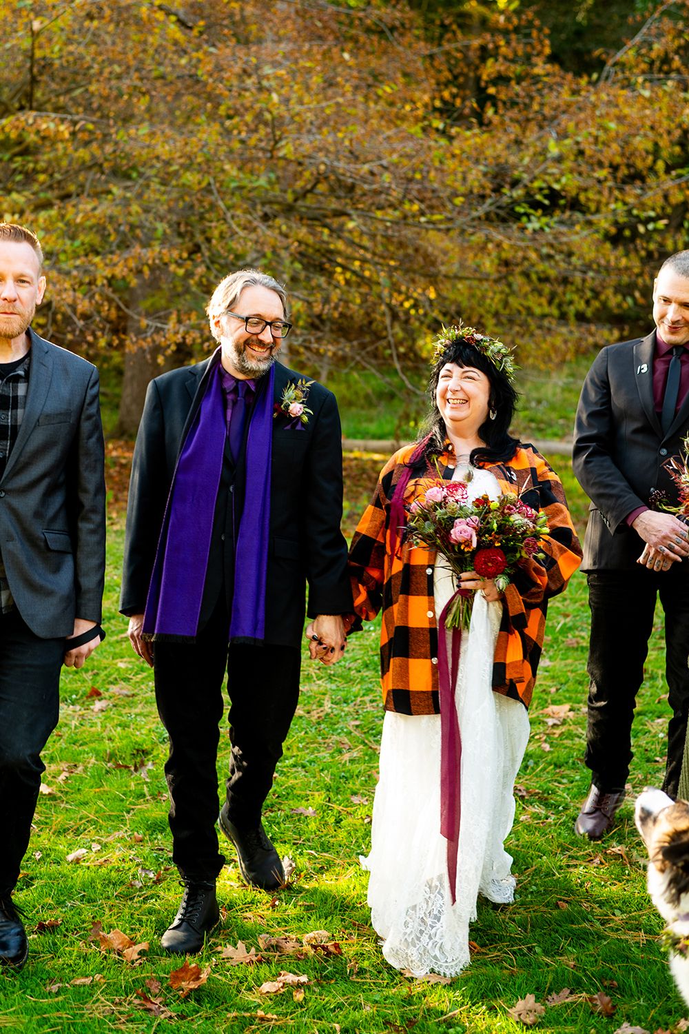 Wedding party celebrates in autumn setting with purple and orange accents in their formal attire.