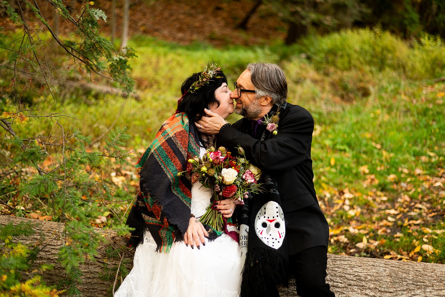A couple enjoys a romantic moment surrounded by autumn foliage and trees in a woodland setting.
