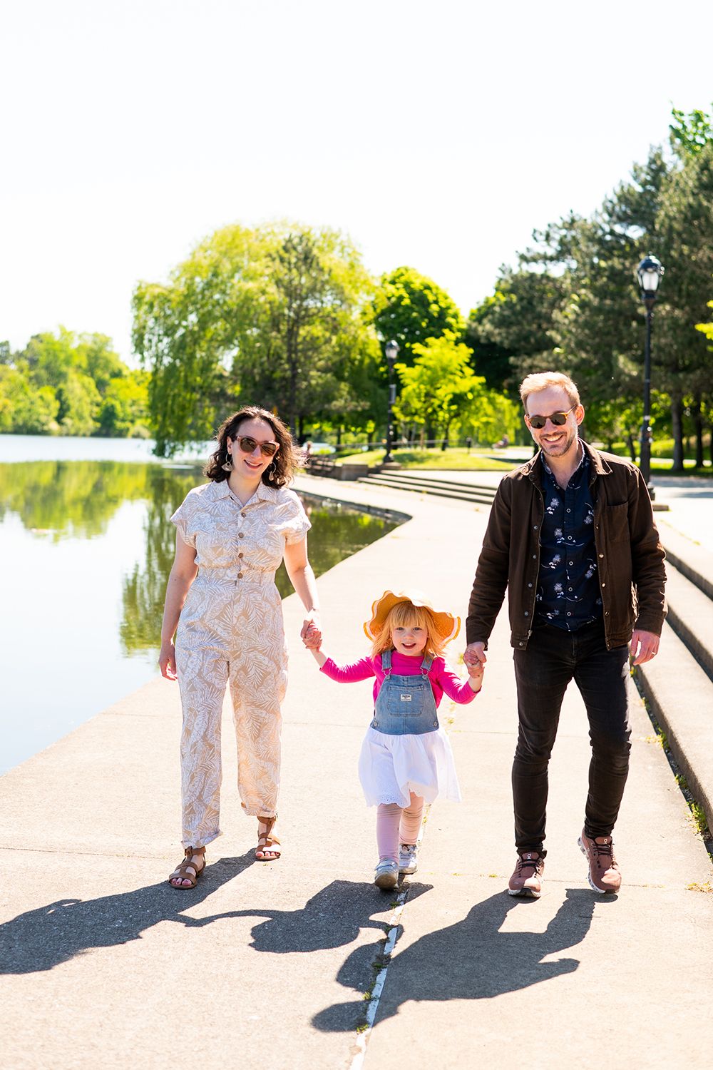 Family walking together on a path next to a scenic lake on a sunny day.