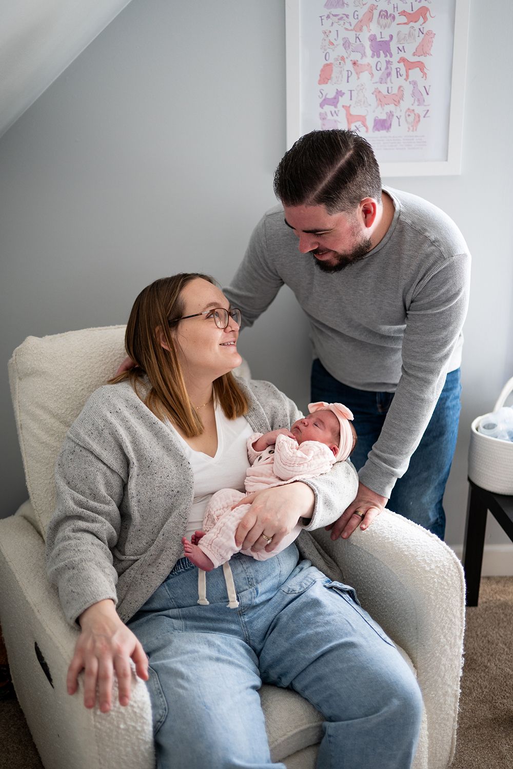 A couple sitting on a gray couch shares joyful moments with their newborn baby while colorful nursery art decorates the wall.