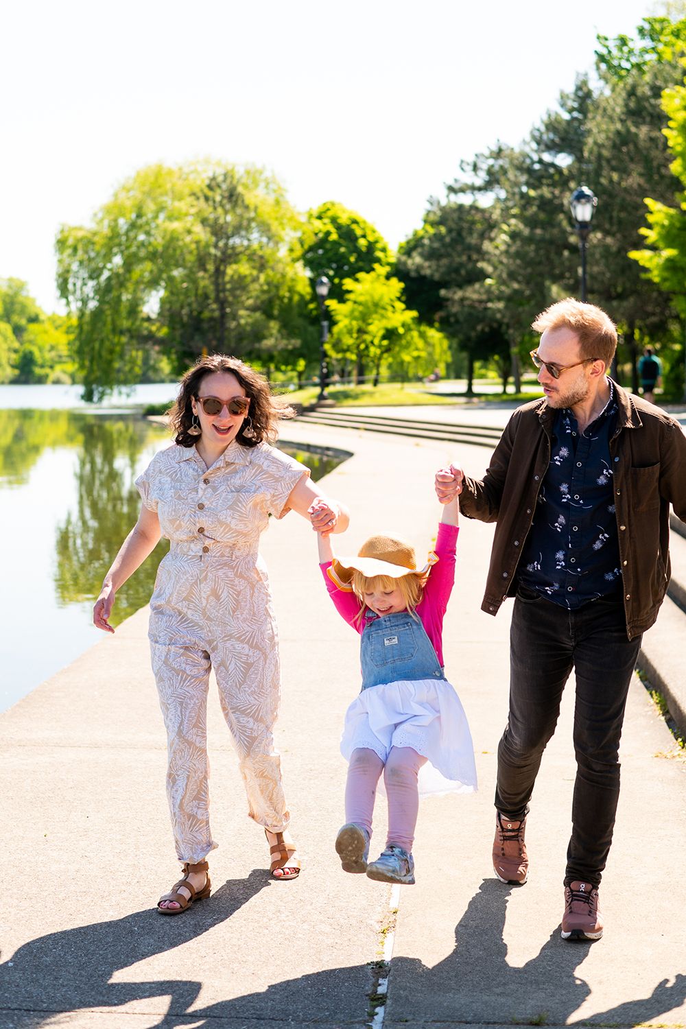 Family enjoying a sunny walk along a waterfront path while holding hands with their toddler.