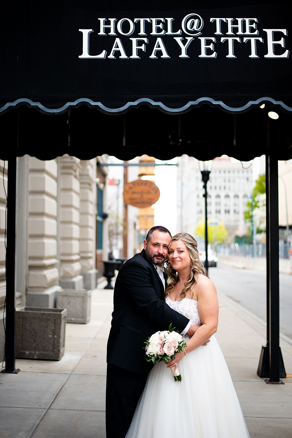 A wedding couple poses outside the entrance of Hotel at the Lafayette in Buffalo with the historic building signage visible.