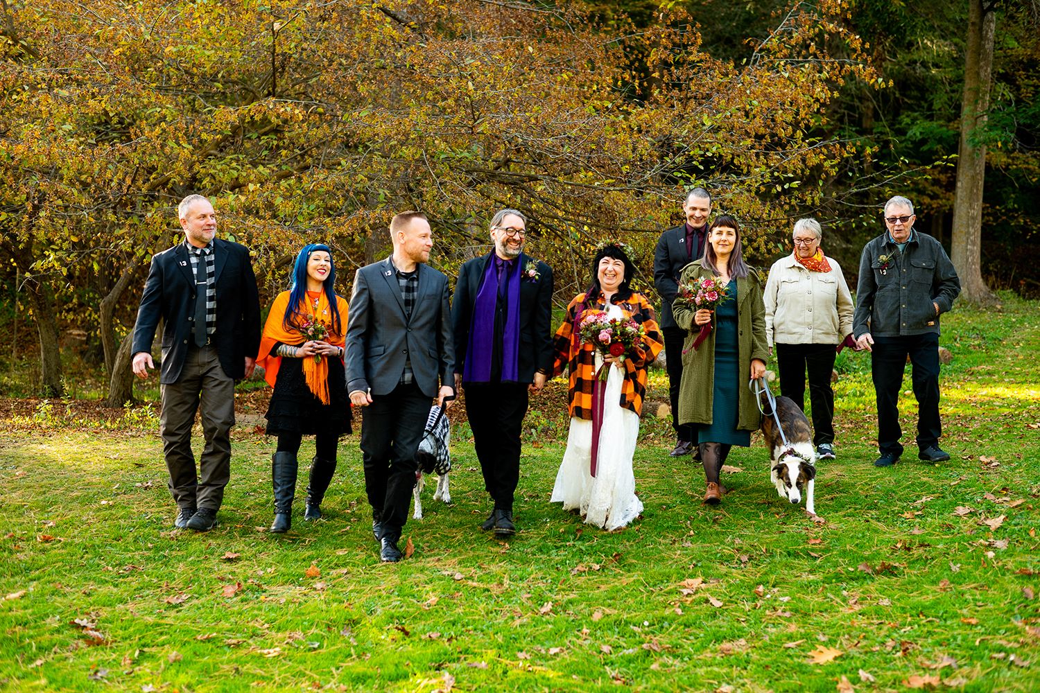 Wedding guests walk across a grassy lawn on a fall day during an outdoor ceremony.