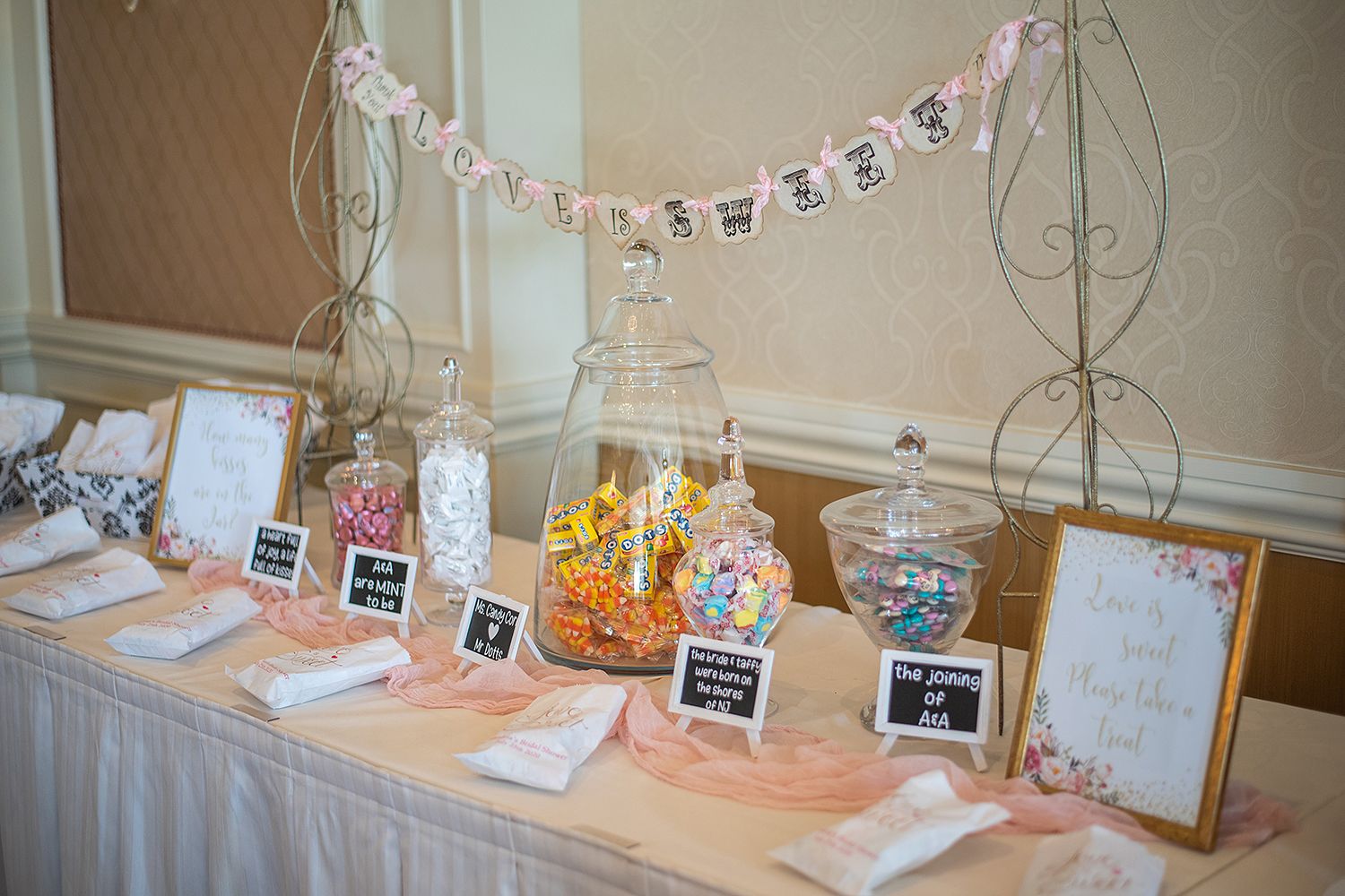 Wedding favor display table with pastel decorations and wire ornaments against beige walls.
