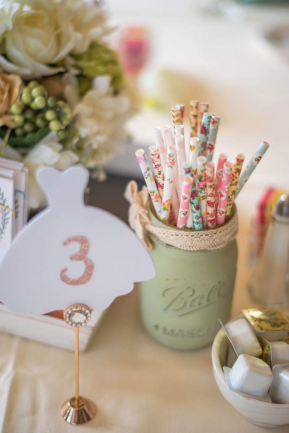 Vintage mason jar filled with decorative floral paper straws and table number three for wedding reception decor.