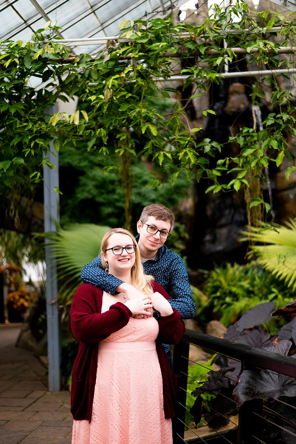 Couple shares romantic moment in lush greenhouse setting with natural lighting.