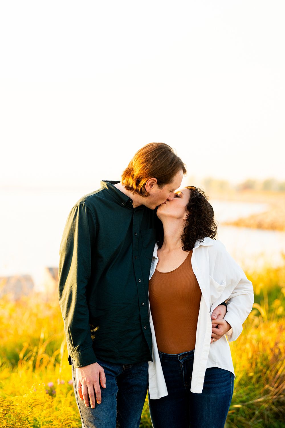 A loving couple shares a tender kiss while standing in a golden field at sunset.
