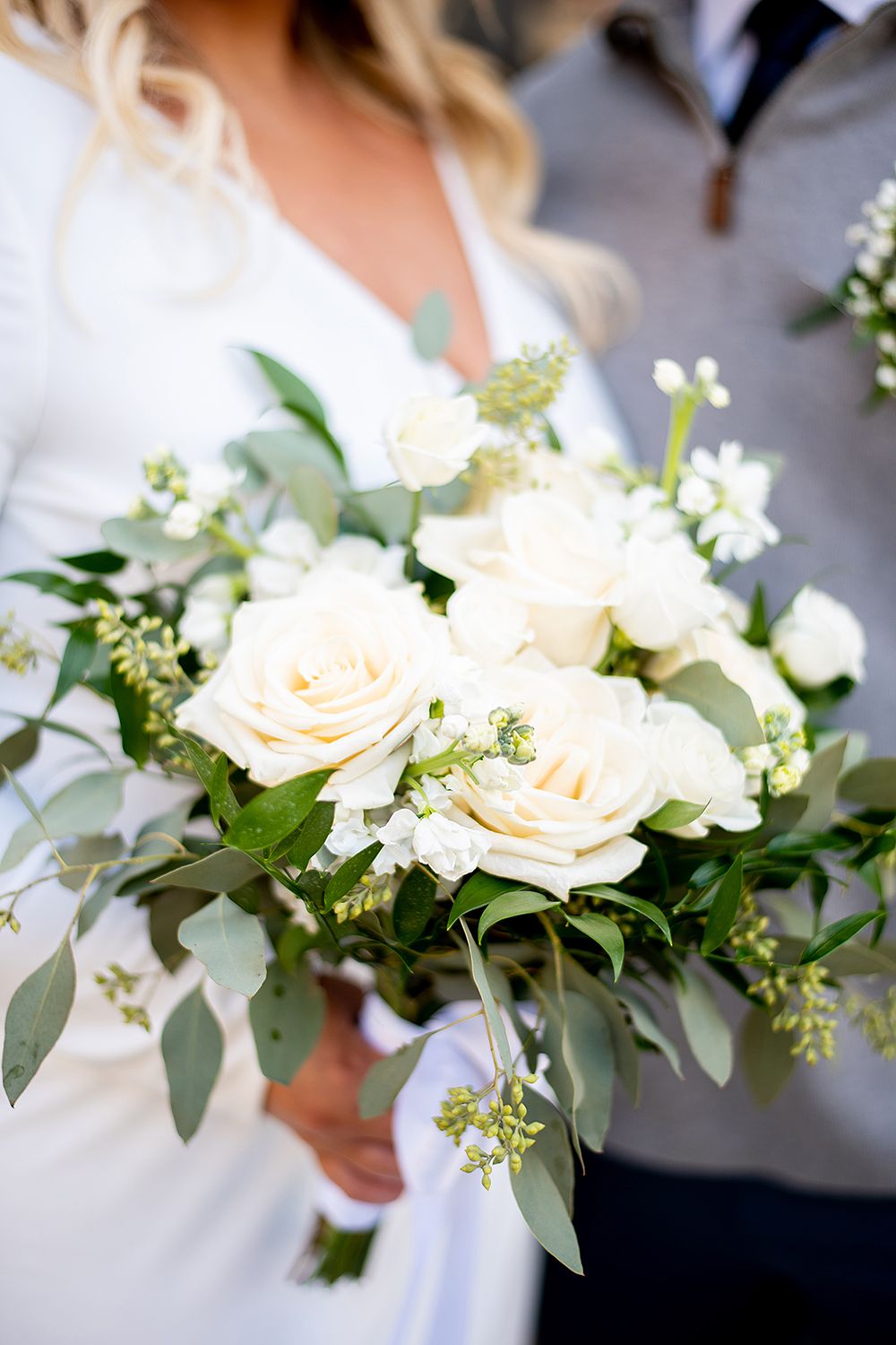 Elegant white rose and eucalyptus bridal bouquet with delicate small flowers and green foliage.