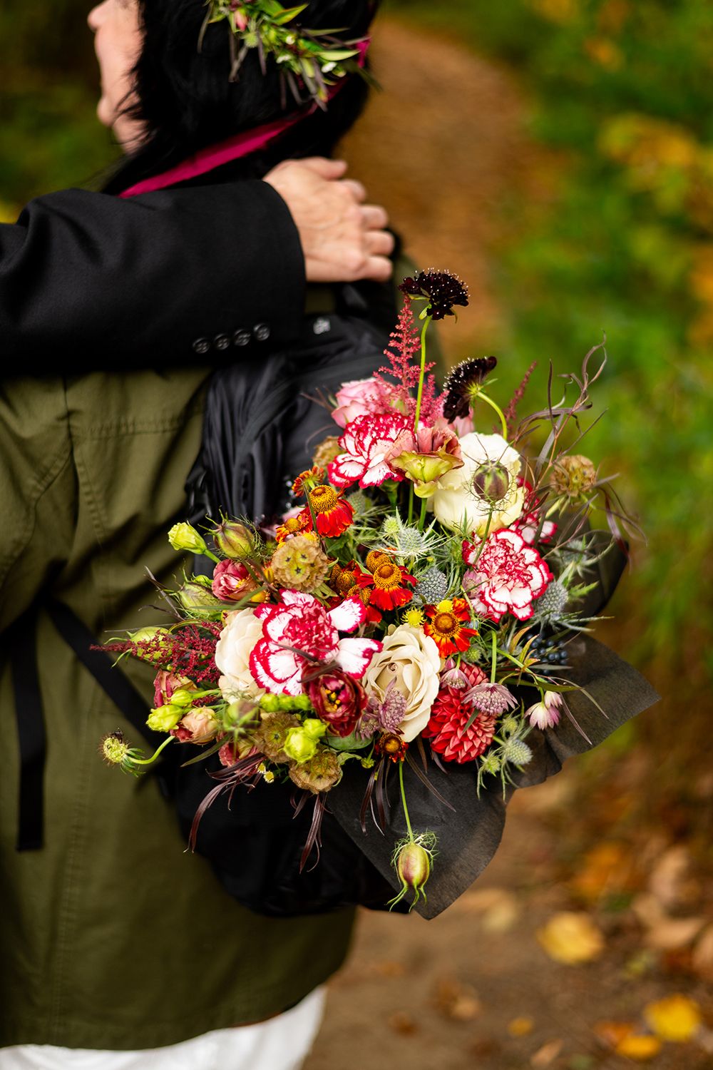 A beautiful autumn bouquet with pink roses, dahlias and wildflowers held against a blurred outdoor background.