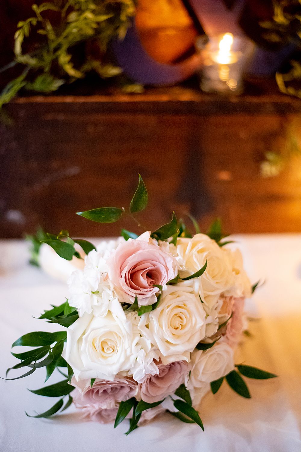 Romantic light pink and white roses with green leaves create an elegant floral display in ambient candlelight.