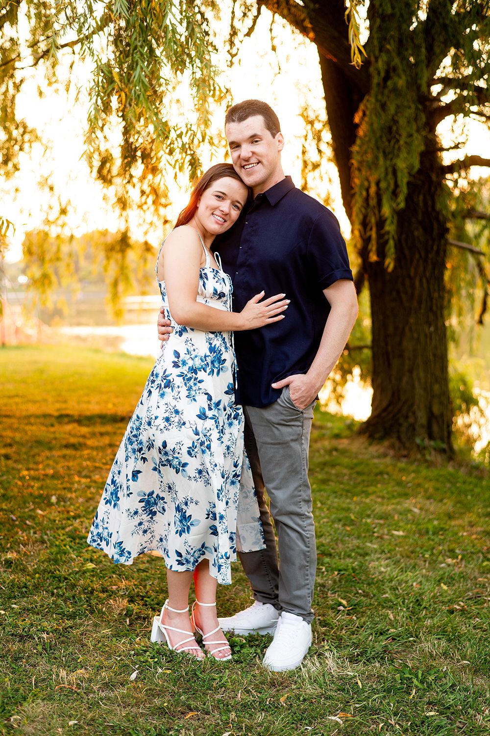 A couple shares a joyful moment under a weeping willow tree at sunset.