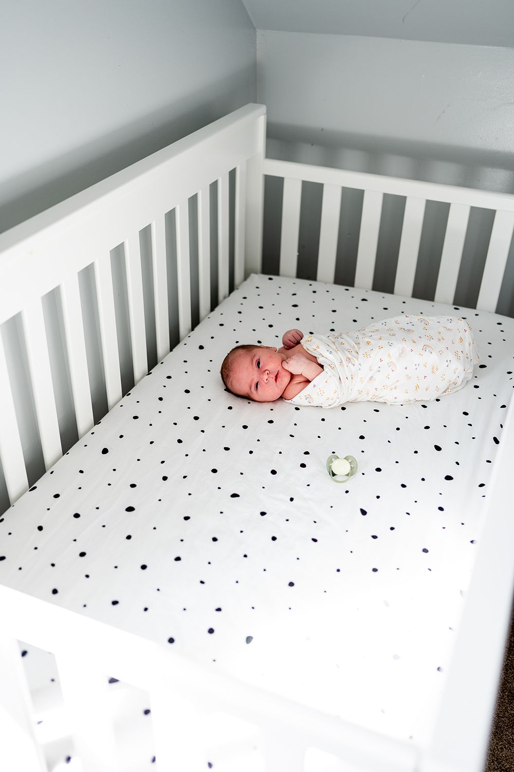 A white crib with polka dot sheets showing different views of a sleeping newborn baby.