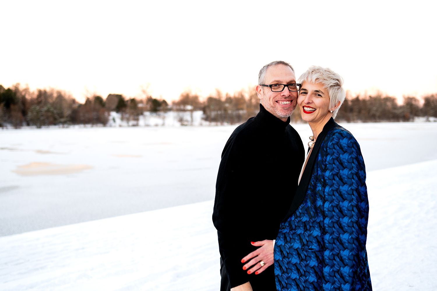 A couple walking together in a serene winter landscape with snowy fields stretching to the horizon.