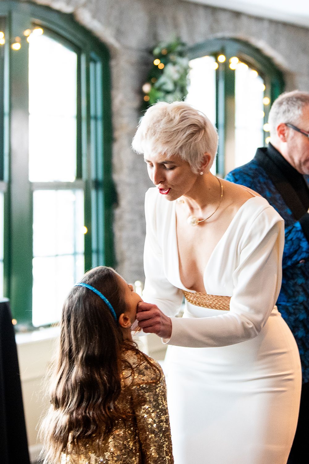 An elegant celebration in a room with arched windows features two people in formal attire interacting during a special moment.
