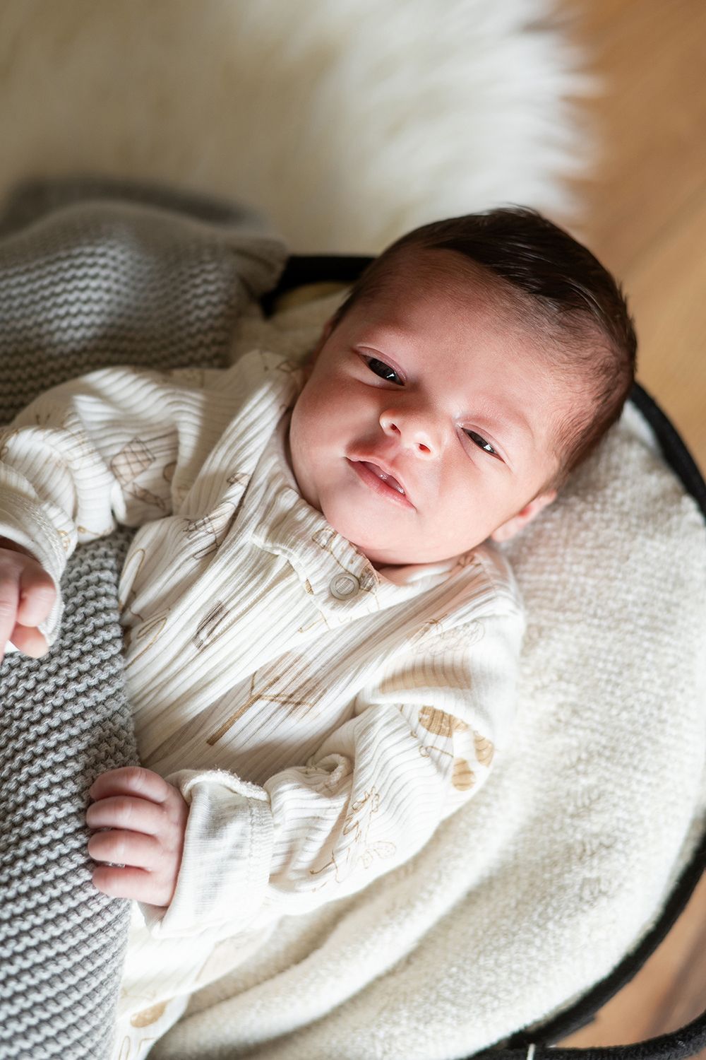 A newborn baby in white clothing lies peacefully on a cozy gray and white blanket.